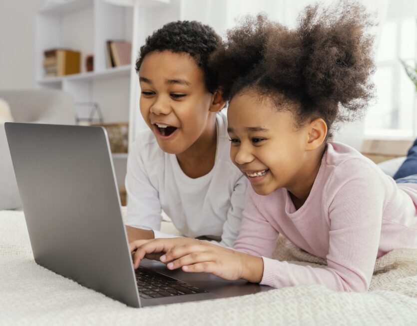 side-view-two-siblings-home-together-playing-laptop