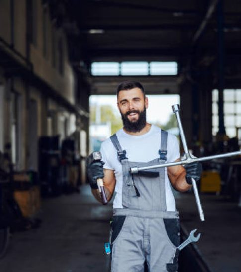 An auto-mechanic is standing in his workshop and holding tools. He is ready to repair trucks, cars, and buses. Worker in the auto-mechanic workshop